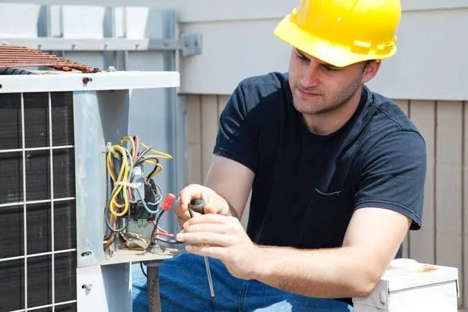 Technician testing wiring on outdoor heat pump equipment
