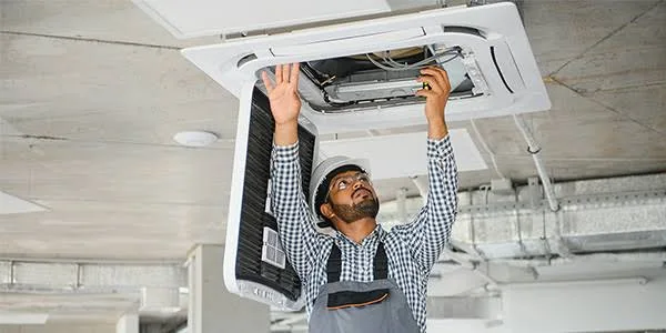 Technician installing ceiling-mounted heating and cooling equipment